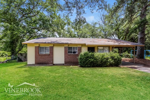 a small brick house with a grassy yard and trees